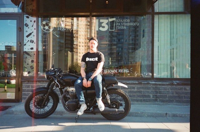 Muž sedí na motorke pred presklenou krčmou.jpg